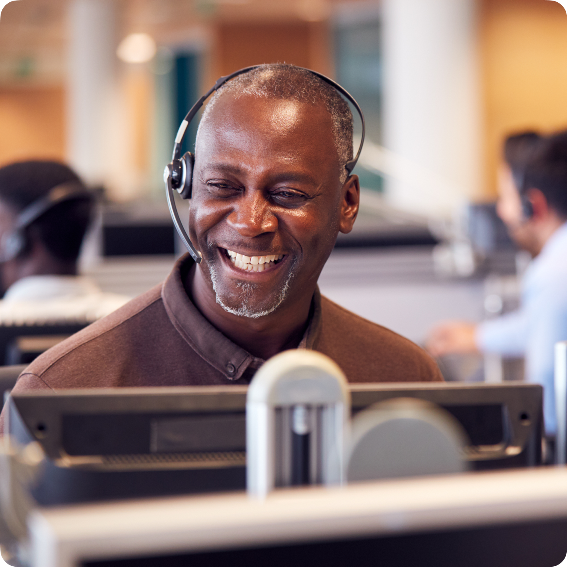 BIPOC customer service representative in a call center. They are wearing a handsfree headset and smiling.