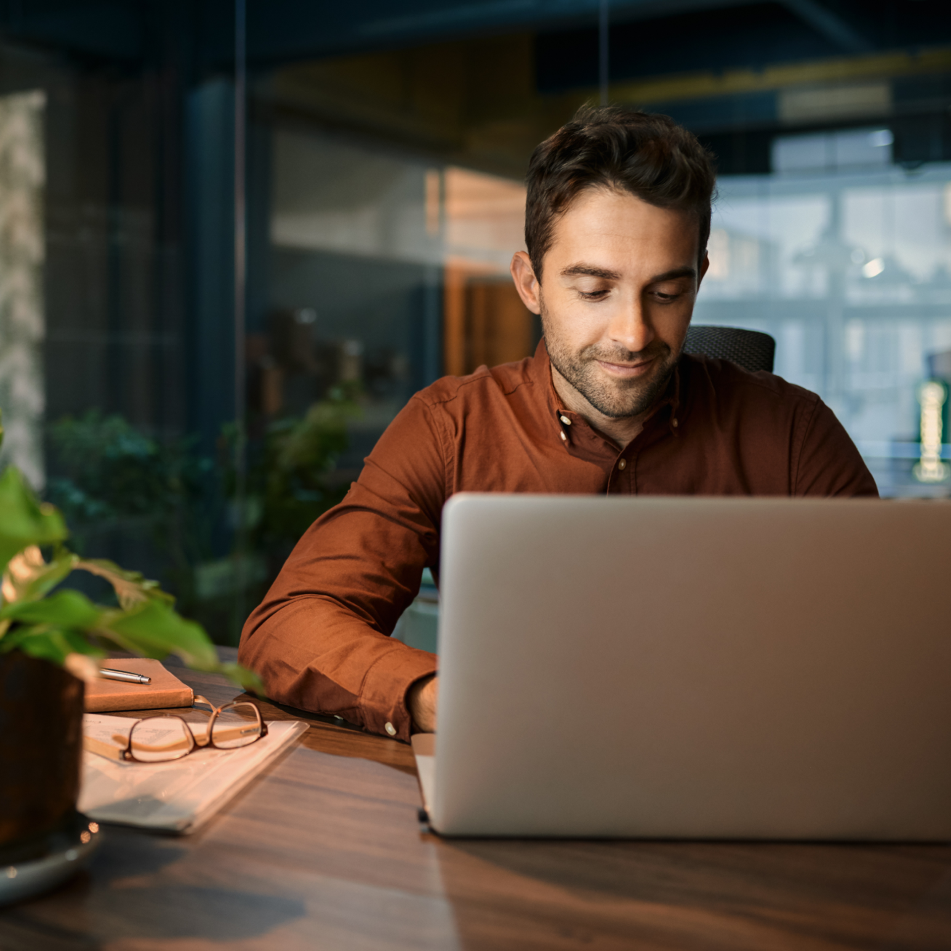 A male-presenting person in a modern office, looking at a laptop.