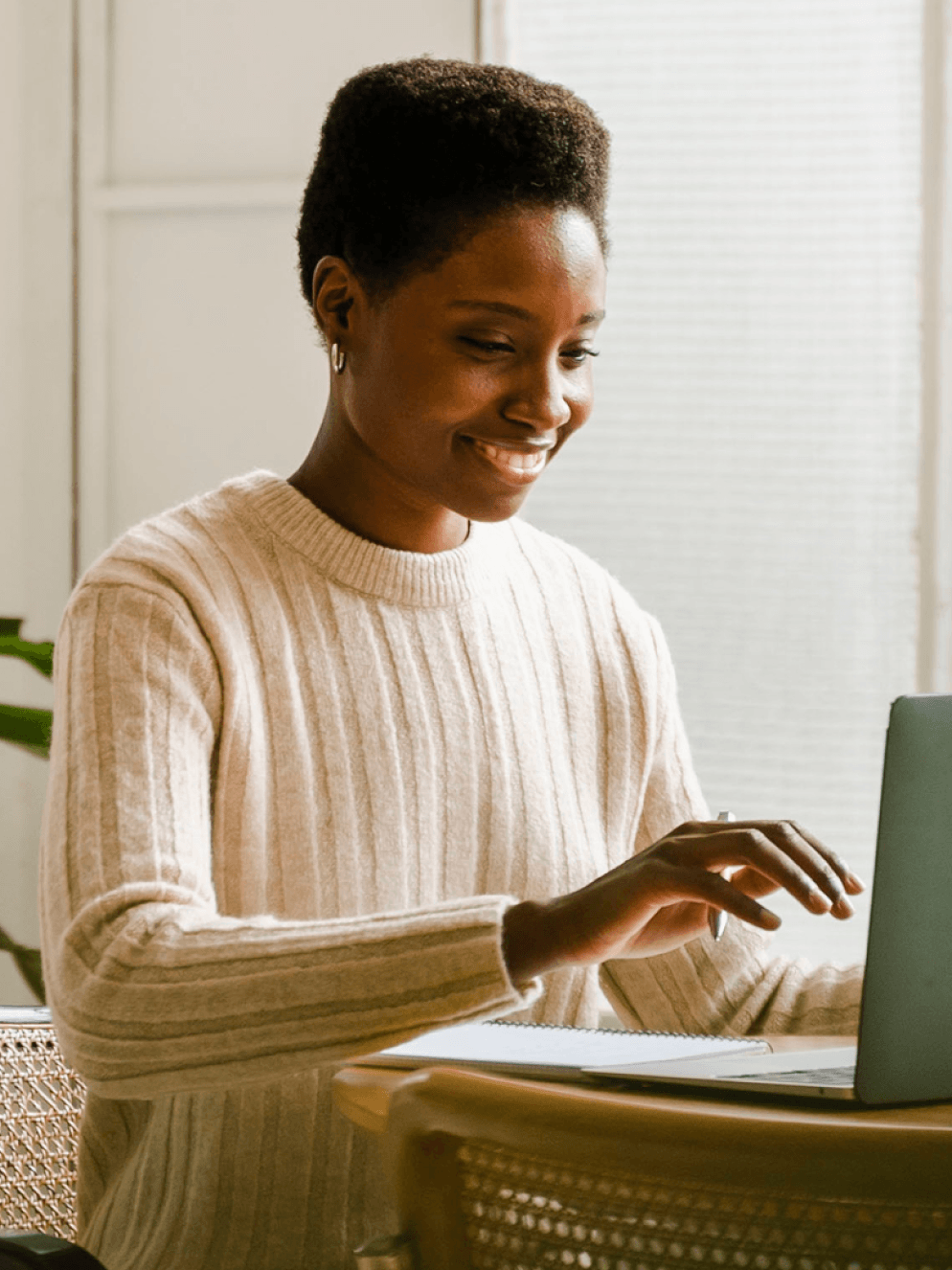 A female-presenting person in a modern room, working on a laptop.