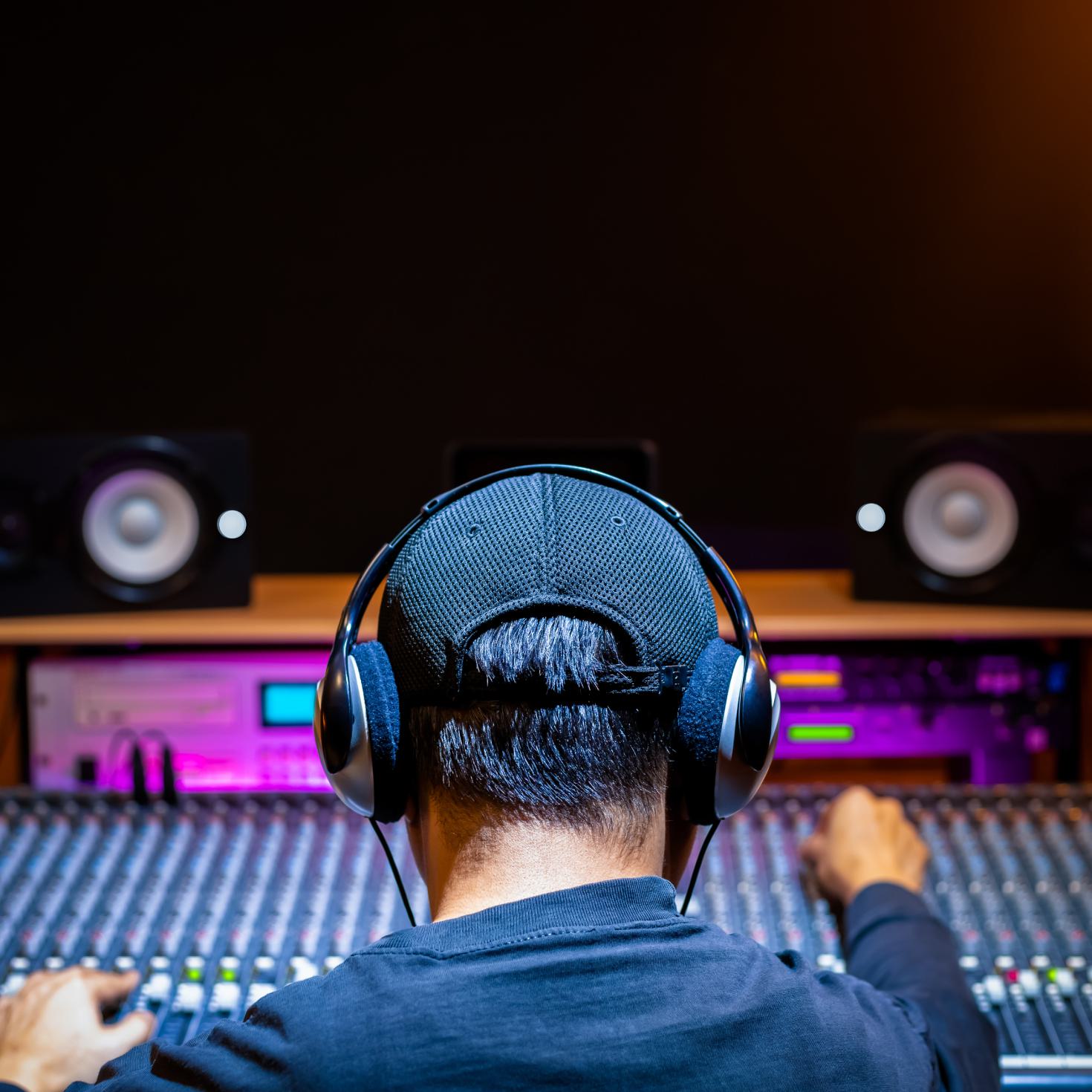 A man in a music studio wearing headphones while adjusting a mixing desk.