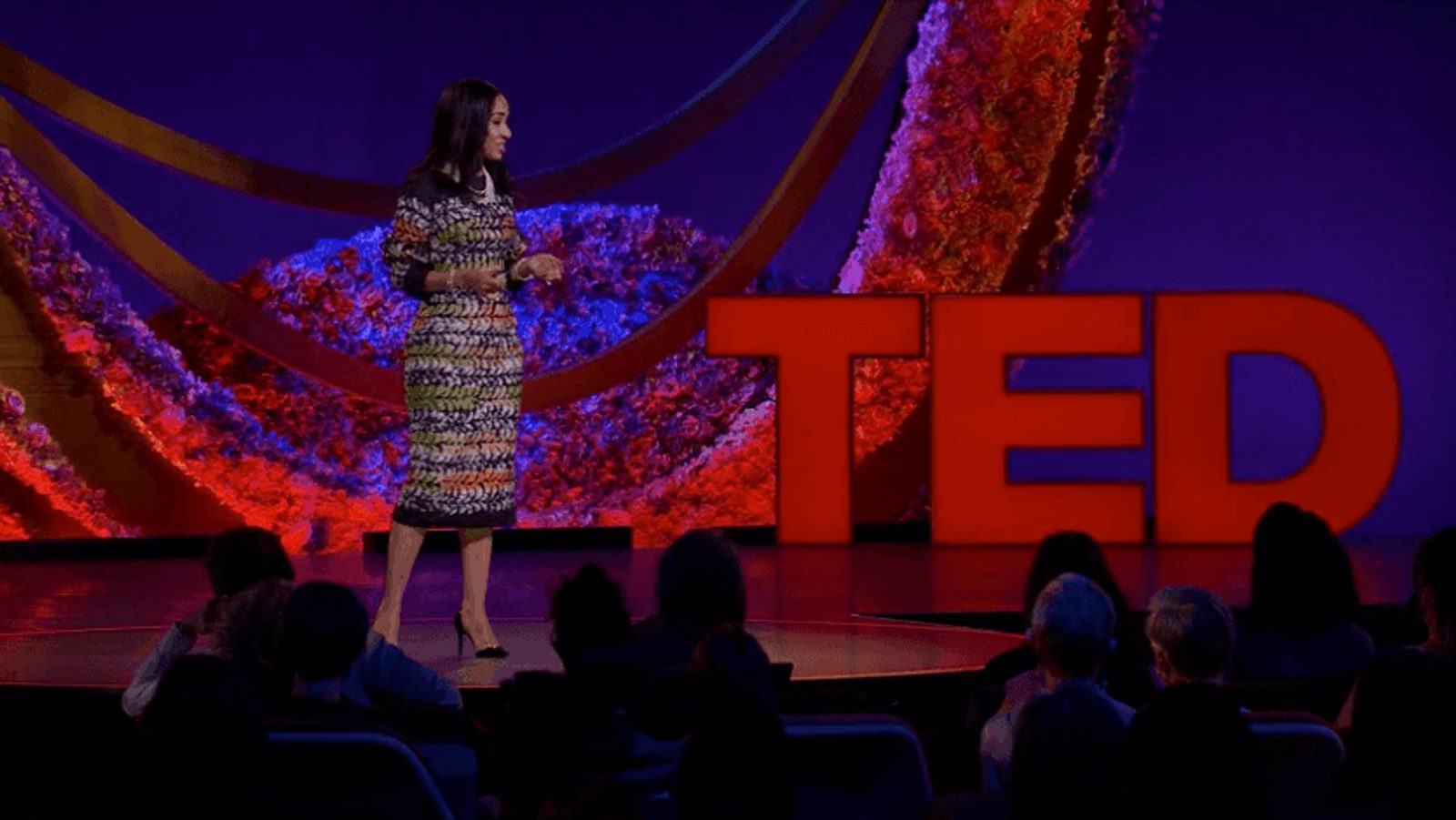 A woman standing onstage with an audience and the word "TED" in the background